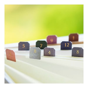 May include: Close-up of a set of colorful index tabs with numbers 1, 4, 5, 7, 8, 9, 12, and 8. The tabs are arranged in a row on a white surface.