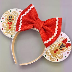 Puede incluir: Diadema con lazo rojo y blanco con orejas de hombre de jengibre. Los hombres de jengibre están decorados con purpurina dorada y chispas rojas y verdes.