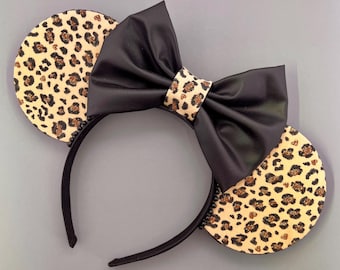 May include: Leopard print mouse ears headband with a black satin bow. The headband is black and the ears are covered in a brown and gold leopard print fabric.