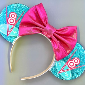 May include: A pair of turquoise blue and pink Minnie Mouse ears with a pink bow and a turquoise blue and white  "Flo's V8 Cafe" logo on each ear.