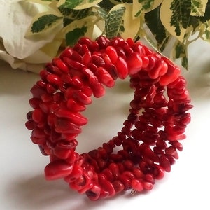 Puede incluir: Un brazalete de coral rojo hecho de peque&ntilde;as cuentas de forma irregular. El brazalete est&aacute; apilado con m&uacute;ltiples filas de cuentas.