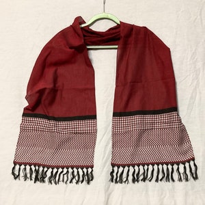 May include: A maroon scarf with black and white geometric patterns and black tassels.