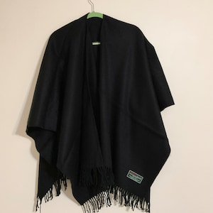 May include: A black wool shawl with fringe on the bottom edge. The shawl is hanging on a green hanger. The label on the shawl reads "100% Pure Wool Made in Italy"