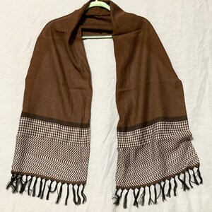 May include: A brown scarf with a white and brown geometric pattern on the ends. The scarf has black tassels.