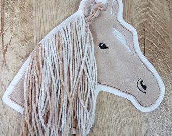 May include: A brown felt horse head with a white felt stripe on its face. The horse has a long mane made of brown and white yarn.