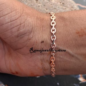 May include: A rose gold chain bracelet featuring oval-shaped links with a textured, etched pattern on the surface. The bracelet is displayed on a wrist, and the text Ramajewellerystore is visible in black script lettering near the center of the chain.