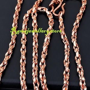 May include: A rose gold-toned chain necklace featuring a twisted rope link design with a polished finish and a circular clasp closure. The text "Ramajewellerstore" is visible in green lettering across the center of the metallic chain links.