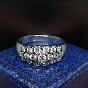 May include: A silver ring with a cluster of clear round stones set in a flower-like design.