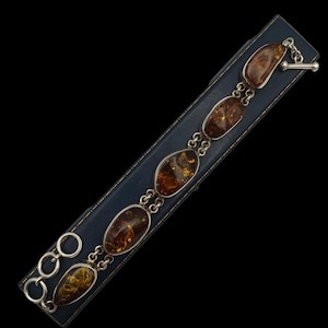 May include: A link bracelet featuring five polished, oval-shaped amber stones set in silver-toned metal frames. The bracelet includes a toggle clasp closure with a circular ring and a T-bar component, connected by small silver-toned metal links.