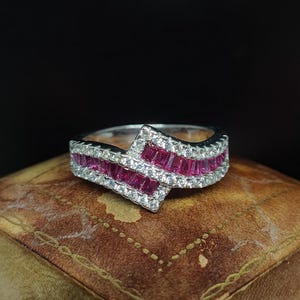 May include: A silver ring with a diamond-shaped centre stone and a row of red ruby stones on each side.