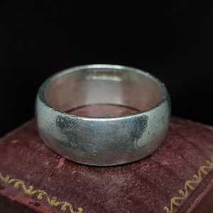 Peut inclure: Une bague en argent avec une surface lisse et arrondie. La bague est posée sur un coffret en velours rouge avec des garnitures dorées.