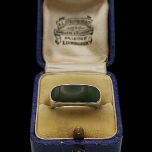 May include: A silver ring with a rectangular, dark green stone, presented in a vintage blue jewelry box with a cream-colored interior. The box is embossed with the text "AL STRUTHERS & CO. JEWELLERS & SILVERSMITHS, DA. LEITH, EDINBURGH."