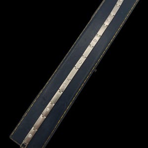 May include: A silver bracelet with small round diamonds set into the metal. The bracelet is on a blue velvet background.