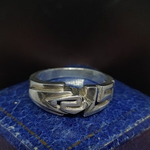 May include: A silver ring with a geometric design. The ring is on a blue velvet box.
