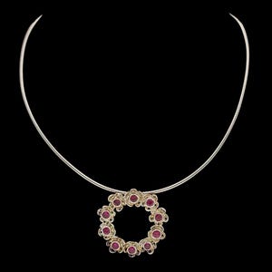 Puede incluir: Un collar de plata con un colgante en forma de círculo. El círculo es de plata y tiene pequeñas piedras preciosas rojas engastadas.