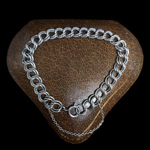 May include: A silver chain bracelet with a lobster clasp. The bracelet is on a brown velvet background.