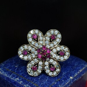 Peut inclure: Une bague en argent avec un motif de fleur. La fleur est composée de pierres blanches et roses.