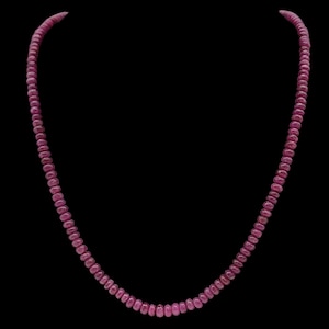 Op de afbeelding: Een ketting bestaande uit kleine, ronde, robijnkleurige kralen. De kralen zijn aan elkaar geregen tot een doorlopende streng, waardoor een eenvoudig maar elegant sieraad ontstaat. De achtergrond is effen zwart, waardoor de ketting wordt benadrukt.