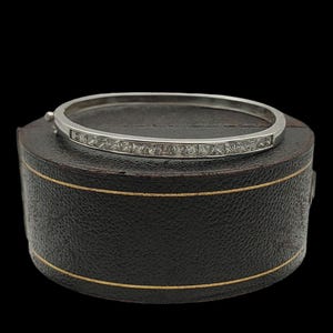 May include: A silver bangle bracelet with a row of clear square-shaped stones set in the metal.