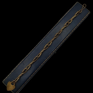 May include: A gold-toned metal chain bracelet featuring alternating smooth oval links and twisted rope-style links. The bracelet terminates with a heart-shaped padlock charm at one end and a small hook-style clasp at the other end.
