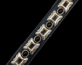 May include: A silver-toned bracelet with black onyx stones and a dark blue leather band. The bracelet features a series of geometric shapes and oval-shaped stones. The clasp is silver-toned. The bracelet is displayed against a black background.