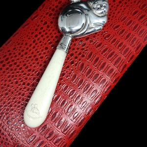 May include: A silver baby rattle shaped like a cat with a white bone handle. The handle has a small engraved image of a rocking horse.