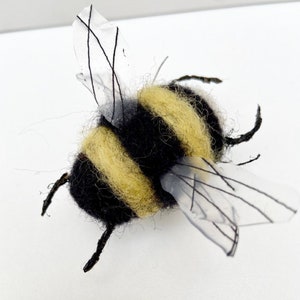 May include: A black and yellow felt bumble bee with clear plastic wings. The wings have black veins.