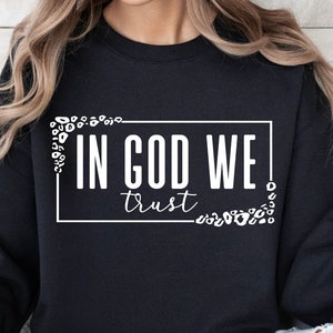 May include: Black sweatshirt with white text that reads "In God We Trust" surrounded by a white frame and white leopard print.