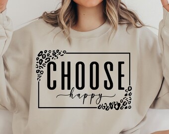Peut inclure: Un sweat-shirt beige avec un graphisme noir qui dit "CHOOSE happy" entouré d'un imprimé léopard noir.