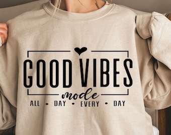 Peut inclure: Un sweat-shirt beige avec un motif noir qui dit "GOOD VIBES mode ALL DAY EVERY DAY" avec un petit cœur noir au-dessus du texte.