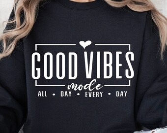 Peut inclure: Sweat-shirt noir avec un texte blanc qui dit "GOOD VIBES mode ALL DAY EVERY DAY" avec un petit cœur au-dessus du mot "VIBES".