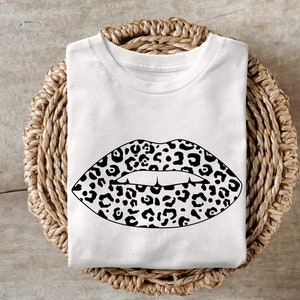 Puede incluir: Camiseta blanca con un diseño de labios de estampado de leopardo en blanco y negro.