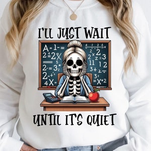 Puede incluir: Sudadera blanca con un profesor esqueleto, una pizarra y el texto "I'll Just Wait Until It's Quiet." El profesor está sentado en un escritorio con un libro, una calculadora y una manzana roja. La pizarra muestra ecuaciones matemáticas.