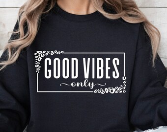 Peut inclure: Sweat-shirt noir avec un texte blanc qui dit "GOOD VIBES only" entouré d'un motif floral blanc.
