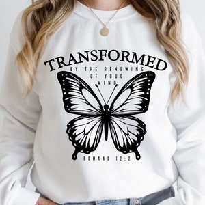 Op de afbeelding: Wit sweatshirt met een zwarte vlinder afbeelding en de tekst "TRANSFORMED BY THE RENEWING OF YOUR MIND. ROMANS 12:2"