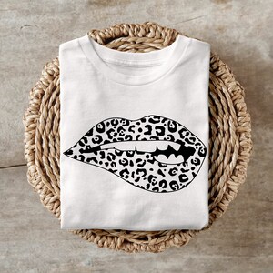 Puede incluir: Camiseta blanca con un diseño de labios de estampado de leopardo en blanco y negro.