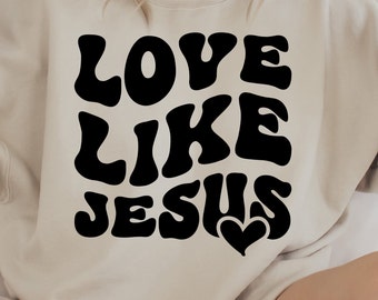 Può includere: Una felpa beige con il testo "LOVE LIKE JESUS" in nero con un piccolo cuore sotto.