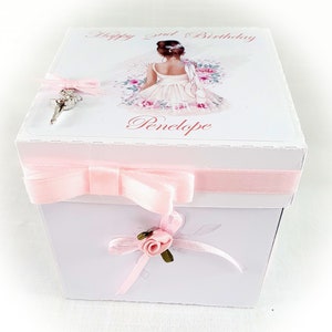 May include: A white box with a pink ribbon and a pink rose. The box has a ballerina illustration on the top with the text "Happy 2nd Birthday Penelope".