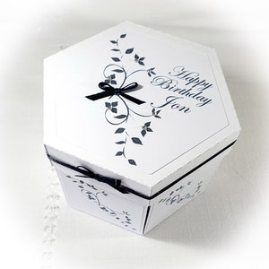 May include: White hexagonal gift box with a black ribbon and a black and white floral design. The box has the text "Happy Birthday Jon" on the top.