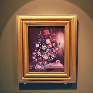 May include: A framed floral still life painting. The artwork features a bouquet of colorful flowers in a vase, set against a dark background. The frame is gold-colored, adding a classic touch to the piece.