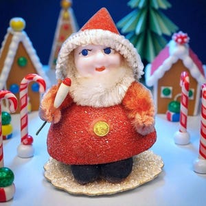 May include: A vintage Santa Claus figurine with a red coat, white fur trim, and a matching hat. The figurine holds a small, white object and is surrounded by candy canes and gingerbread houses, evoking a festive Christmas theme.