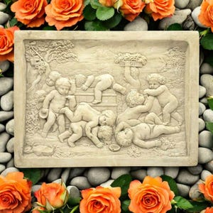 May include: A rectangular stone plaque with a raised relief sculpture of cherubs playing. The cherubs are depicted in various poses, some are climbing on a barrel, others are playing with a bucket, and one is lying down. The plaque is a light beige color and has a rough texture.