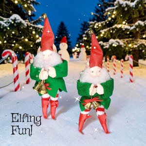 May include: Two Christmas elf figurines with red hats, green jackets, and red and white striped stockings. Each elf holds two golden bells. The text "Elfing Fun!" is at the bottom left of the image. The background includes candy canes, snowmen, and Christmas trees.