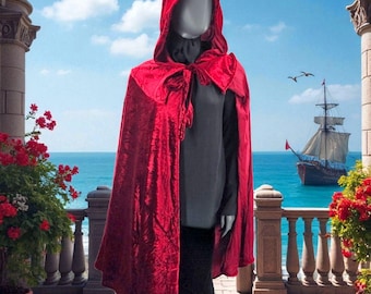 May include: A vibrant red hooded cape with a tie closure. The cape is made of a textured fabric and drapes over a dark outfit. The background features a seascape with a sailing ship and a blue sky.
