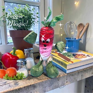 May include: A handcrafted radish figurine with a gradient red and white body, green leafy arms and feet, and a hand-painted face. The radish features a top sprout and stands upright, accented by white star graphics and the text Veggie Magic!