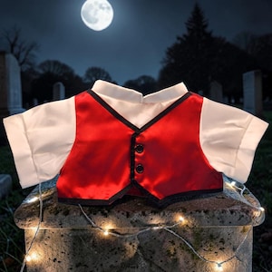 Puede incluir: Un chaleco de satén rojo con ribete negro y tres botones negros, combinado con una camisa blanca con cuello. El atuendo se exhibe sobre una superficie de piedra, con un cementerio y una luna llena de fondo. El tema general es Halloween.