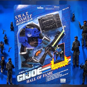 May include: A G.I. Joe Hall of Fame S.W.A.T. Assault Mission Gear action figure set. The set includes a black and blue uniform, a rifle, and a backpack with a fold-down computer. The packaging features the text "A Real American Hero."