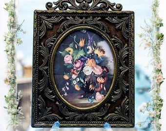 May include: A vintage-style oval picture frame with an ornate gold-toned metal frame. The frame features a floral print with a variety of colorful flowers in a vase.
