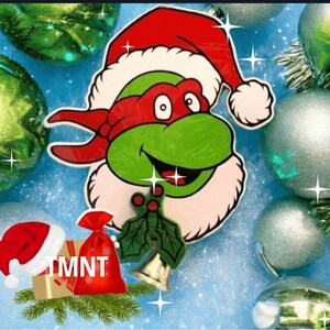 May include: A festive Christmas decoration featuring a Teenage Mutant Ninja Turtle character wearing a Santa hat. The image includes a red gift bag with "TMNT" text, a Santa hat, and Christmas ornaments on a blue background.