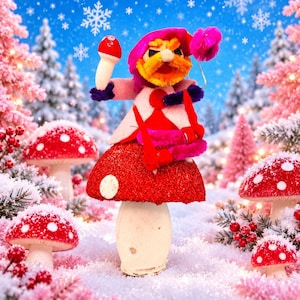 May include: A handcrafted gnome figurine with a bright orange beard and a pink hat, perched atop a large, glittery red mushroom with white spots. The gnome holds a small red mushroom in one hand and a pink pom-pom in the other, wearing a pink jacket.